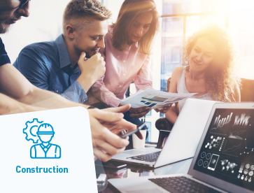 Team collaborates around a table, reviewing construction plans with laptops displaying designs