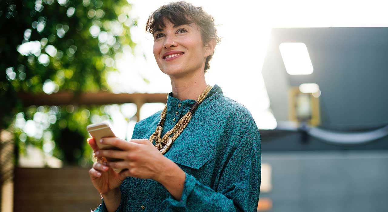 mulher a sorrir com telemóvel na mão representando os consumidores